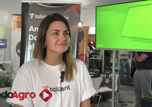 Integrante de Taligent con remera de la marca durante una entrevista en un evento de TodoAgro, con banners de la empresa de fondo
